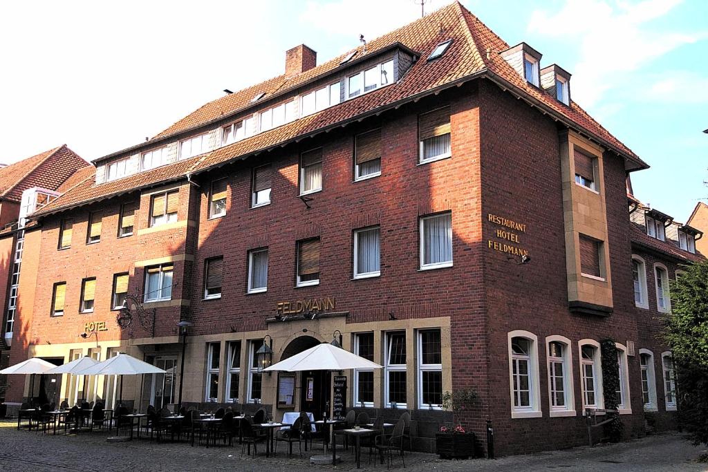 un gran edificio de ladrillo con mesas y sombrillas delante de él en Hotel Feldmann en Münster