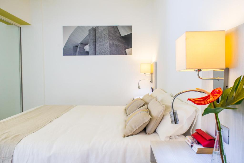 a white bedroom with a bed and a table with a flower at Udalla Park - Hotel & Apartamentos in Playa de las Americas