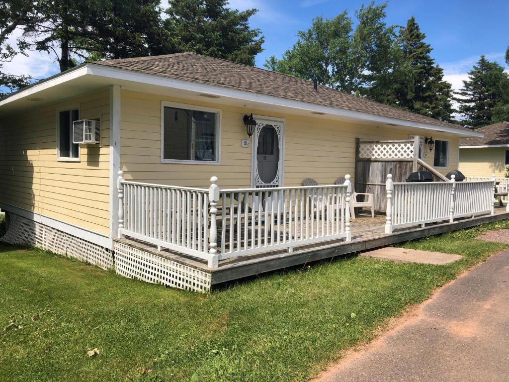 a small yellow house with a wooden deck at Shining Waters - Ingleside Cottages in Cavendish