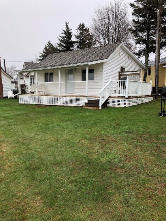 a white house with a porch and a yard at Shining Waters - Ingleside Cottages in Cavendish