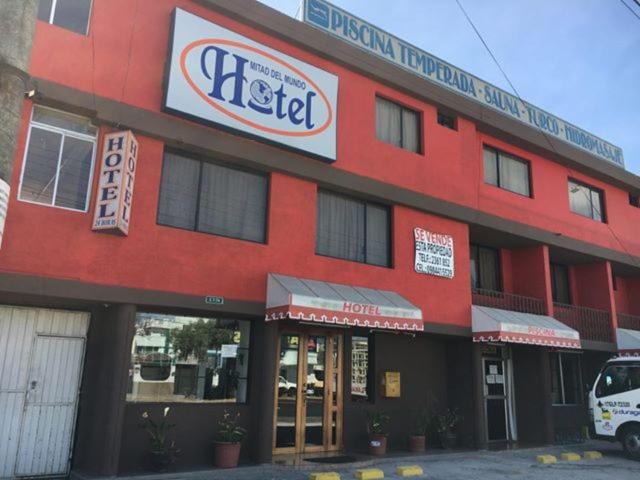ein rotes Gebäude mit einem Schild für ein Hotel in der Unterkunft Hostal Mitad del Mundo in Cayambe