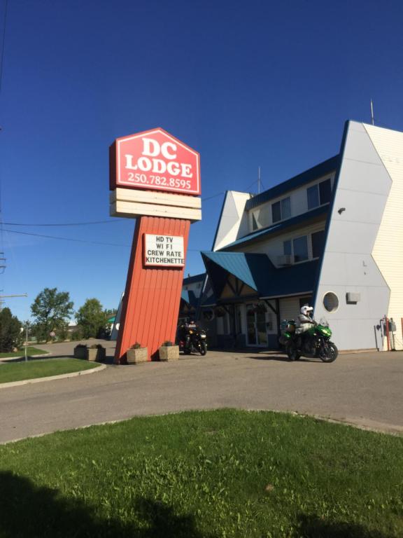 una señal para una cabaña de perros con una motocicleta aparcada delante en DC Lodge, en Dawson Creek