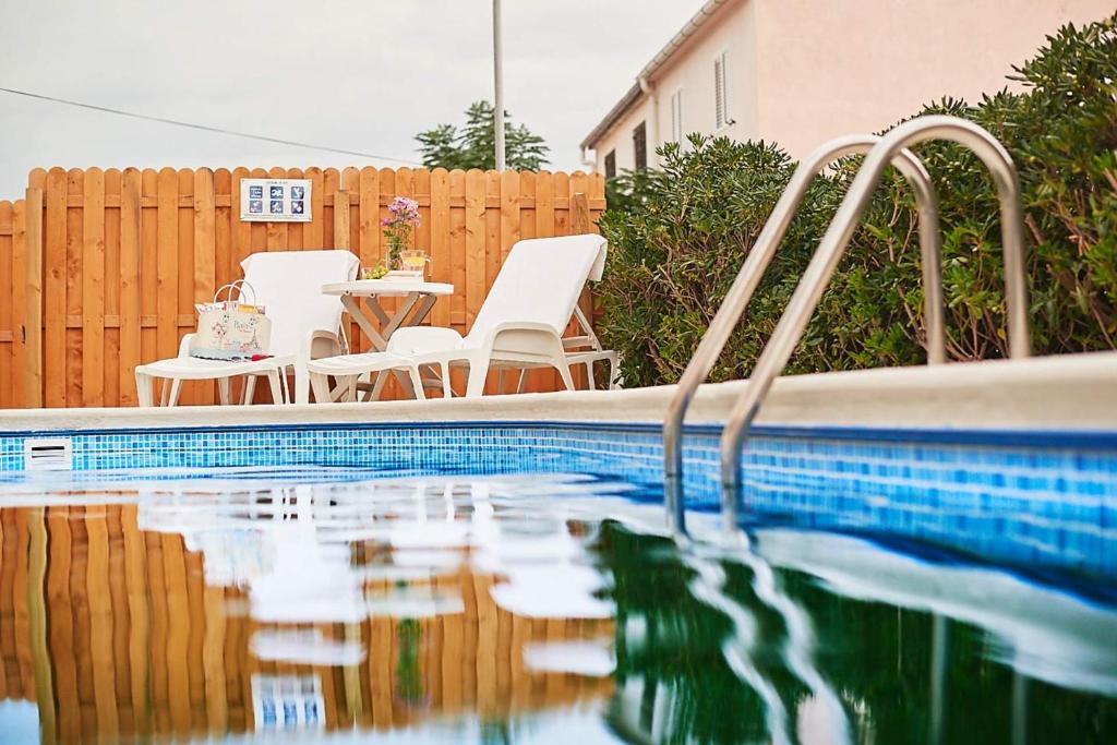 une piscine avec des chaises blanches et une clôture dans l'établissement Apartments Adriapag, à Pag
