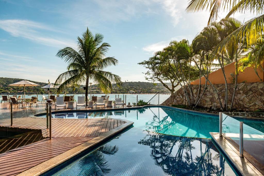 a resort pool with chairs and a view of the water at Hotel Ferradura Private in Búzios