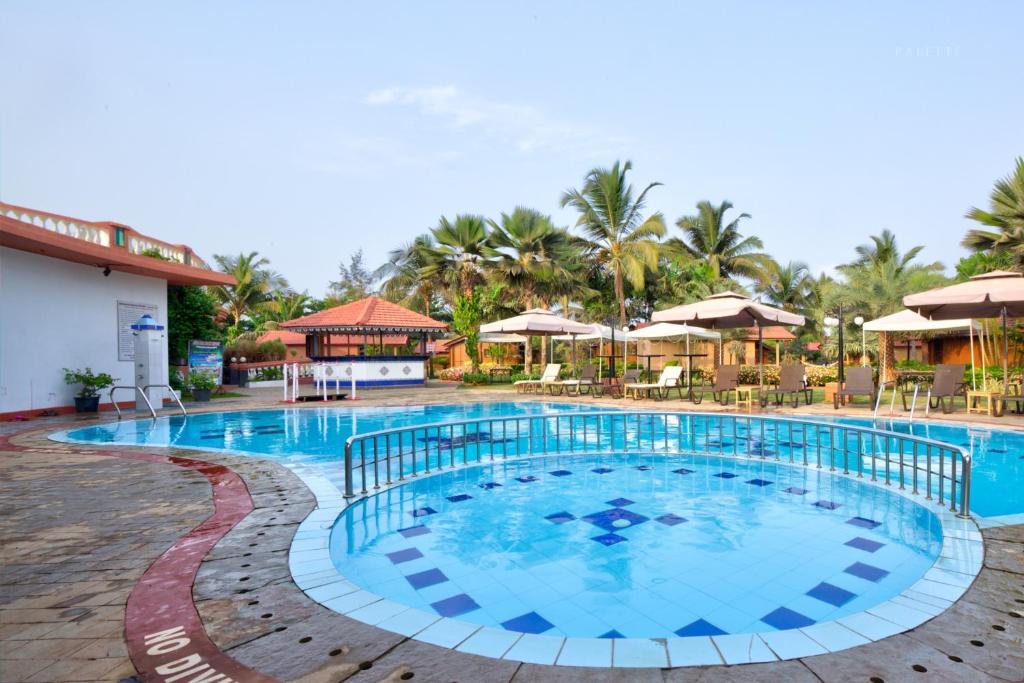 una piscina en un complejo con sillas y sombrillas en Beira Mar Beach Resort, en Benaulim