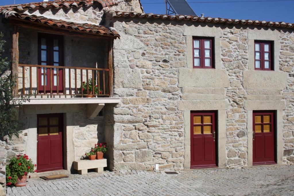 un edificio de piedra con puertas rojas y balcón en Casa de l Bárrio, en Picote