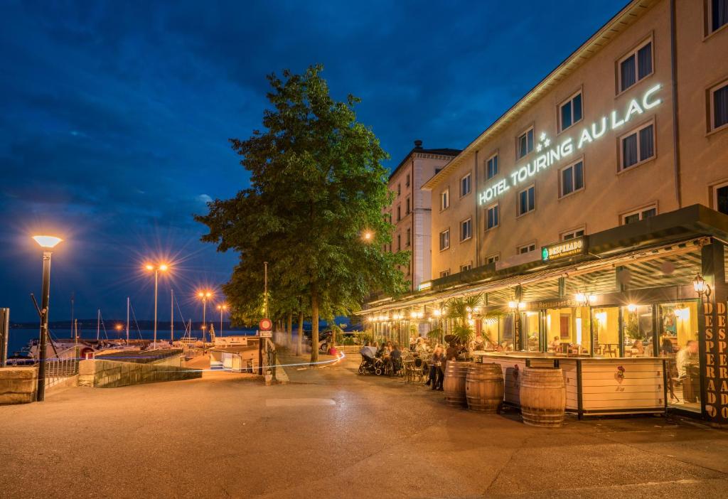 Un bâtiment avec des personnes assises à l'extérieur le soir dans l'établissement Touring au Lac, à Neuchâtel