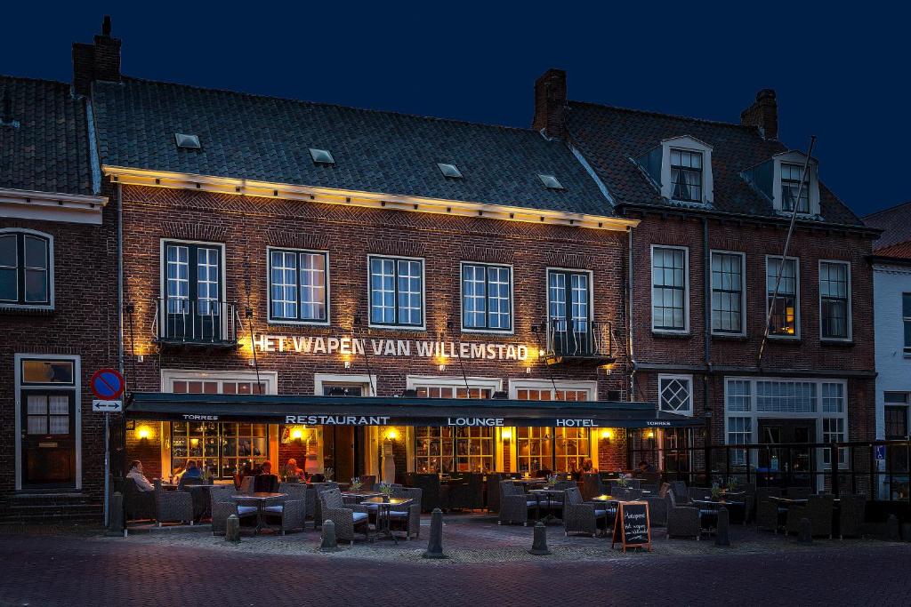 een groot bakstenen gebouw met tafels en stoelen ervoor bij "Het Wapen Van Willemstad" in Willemstad