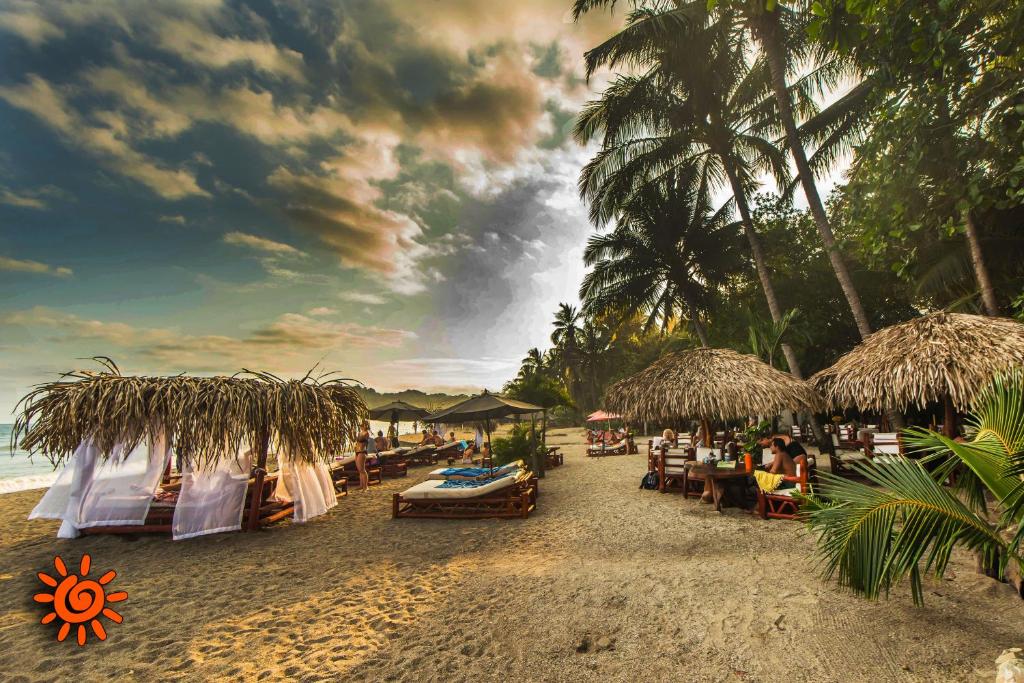 una playa con mesas, sillas y sombrillas y el océano en Locanda Samara Beach, en Sámara