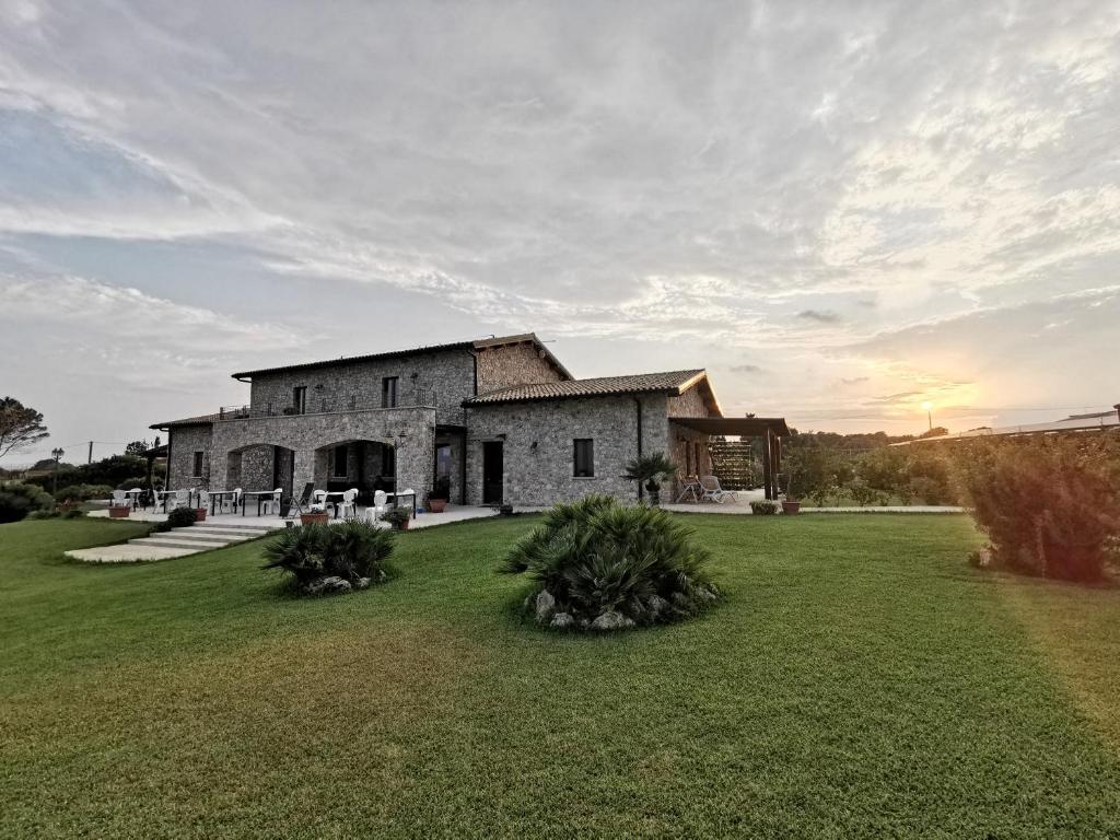 a large stone house with a grass yard at B&B Al Tramonto Portopalo in Portopalo