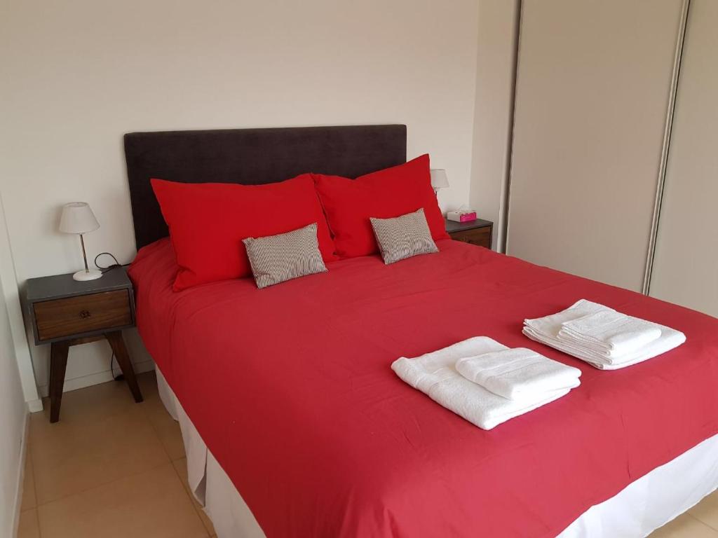 Una cama roja con dos toallas encima. en Departamento Pioneros en San Carlos de Bariloche