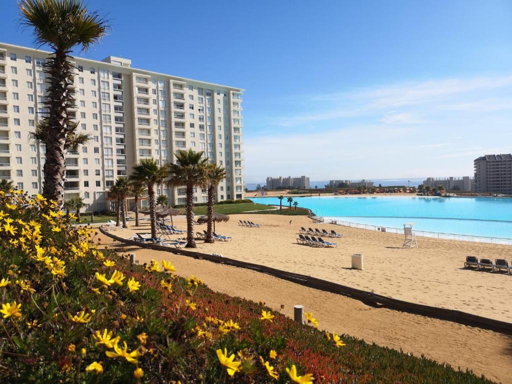 une plage avec des chaises et des palmiers ainsi qu'un grand bâtiment dans l'établissement Departamento en Laguna Bahia, à Algarrobo