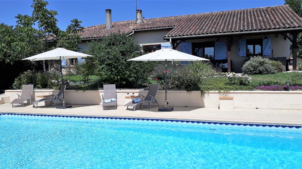 una casa con piscina con sedie e ombrelloni di Gîte Les Volets Bleus a Monflanquin