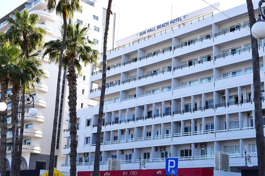 a white hotel with palm trees in front of it at Sun Hall Beach Hotel Apartments in Larnaca