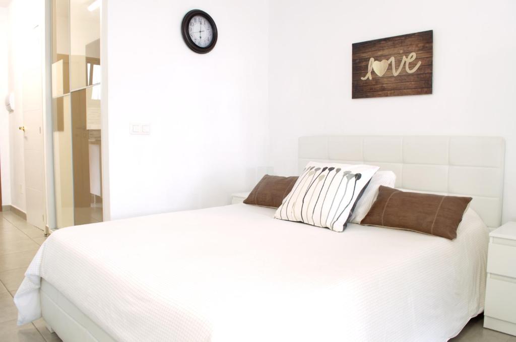 プエルト・デ・ラ・クルスにあるEdificio Seguro de Sol, Puerto La Cruz, Islas Canarias Tenerifeの白い部屋の白いベッド(壁に時計付)