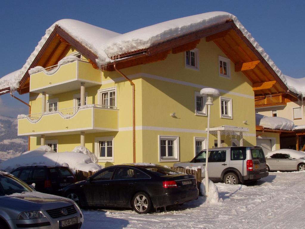 a yellow house with cars parked in the snow at Haus Heigl in Sankt Johann im Pongau