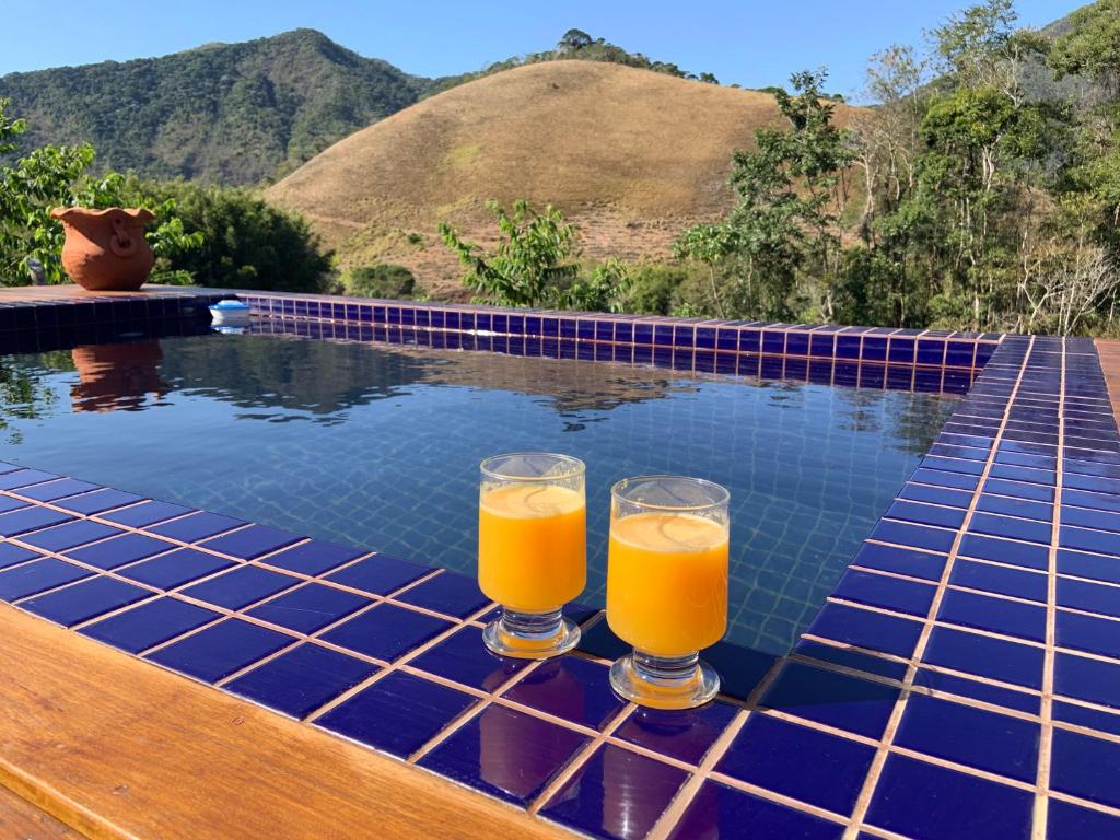 two glasses of orange juice on a table next to a swimming pool at Cactus Chalé em lumiar in Lumiar
