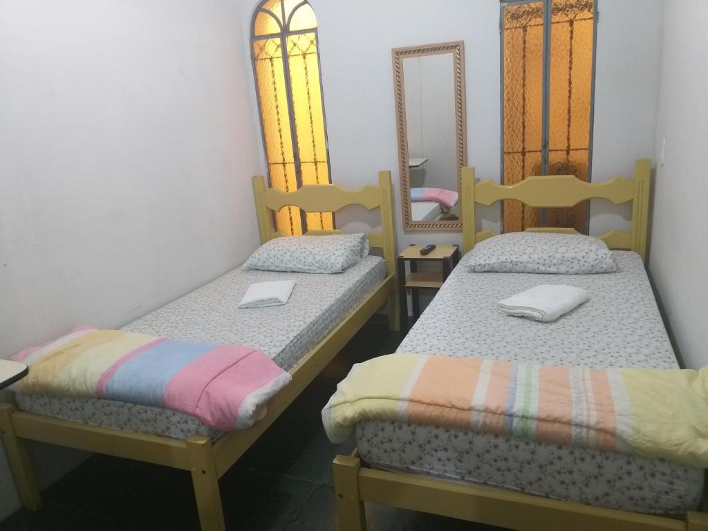 Duas camas individuais num quarto com um espelho. em Pousada Bem Viver 1 em Itaperuna