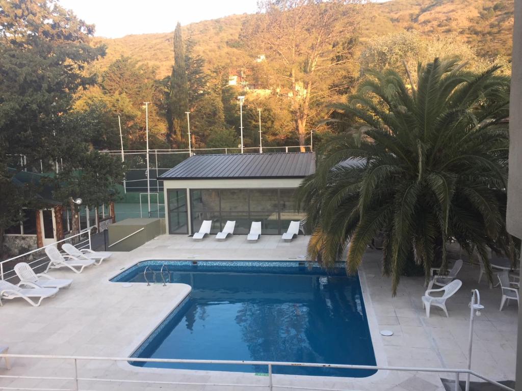 a swimming pool with chairs and a palm tree at Apart-Hotel Gibert's House in Villa Carlos Paz