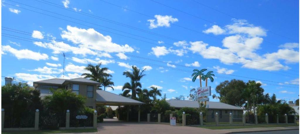 a building with palm trees and a blue sky with clouds at Biloela Palms Motor Inn in Biloela