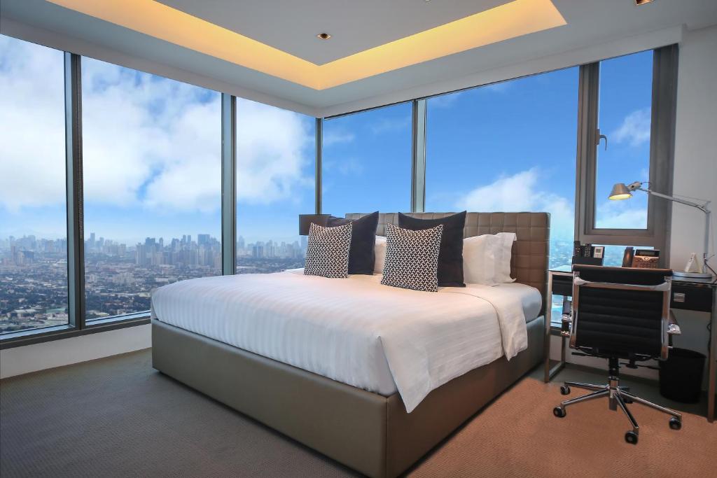 Un dormitorio con una cama, un escritorio y ventanas. en The Alpha Suites, en Manila