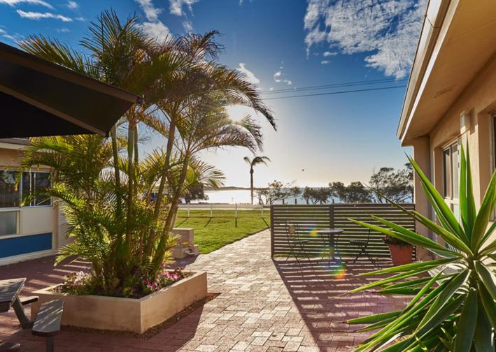 a patio with palm trees and a fence at API Pelican Beach Front Apartments Kalbarri in Kalbarri