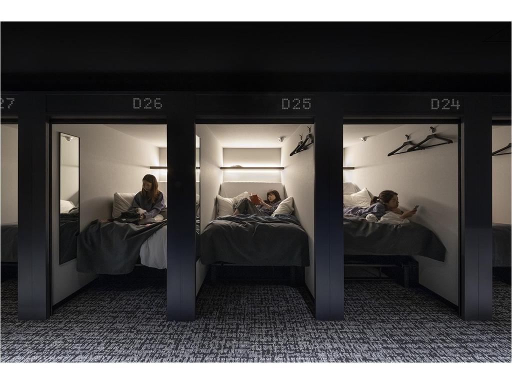 2 Personen auf Betten in einem Zimmer mit Spiegeln in der Unterkunft The Millennials Fukuoka in Fukuoka