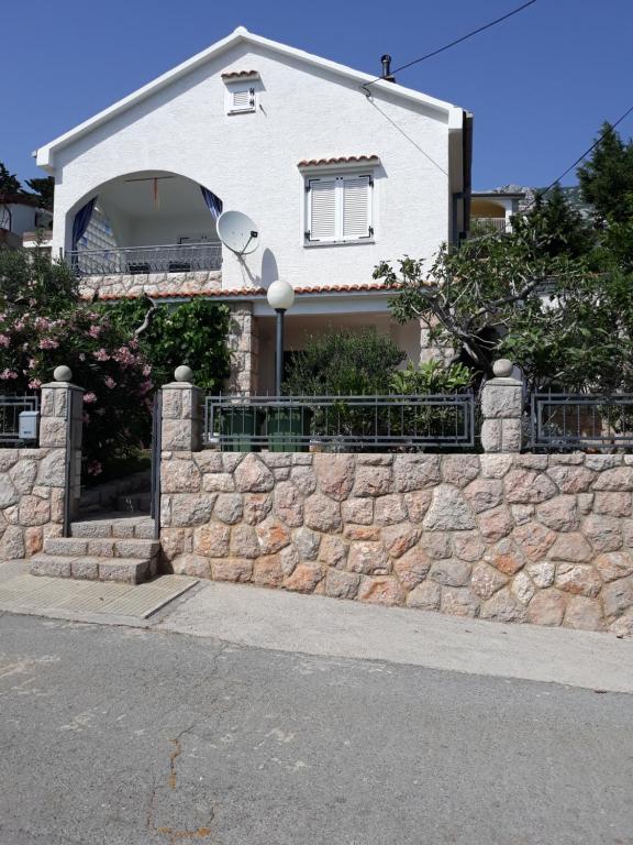 a white house with a stone retaining wall at Apartman Grospic in Cesarica