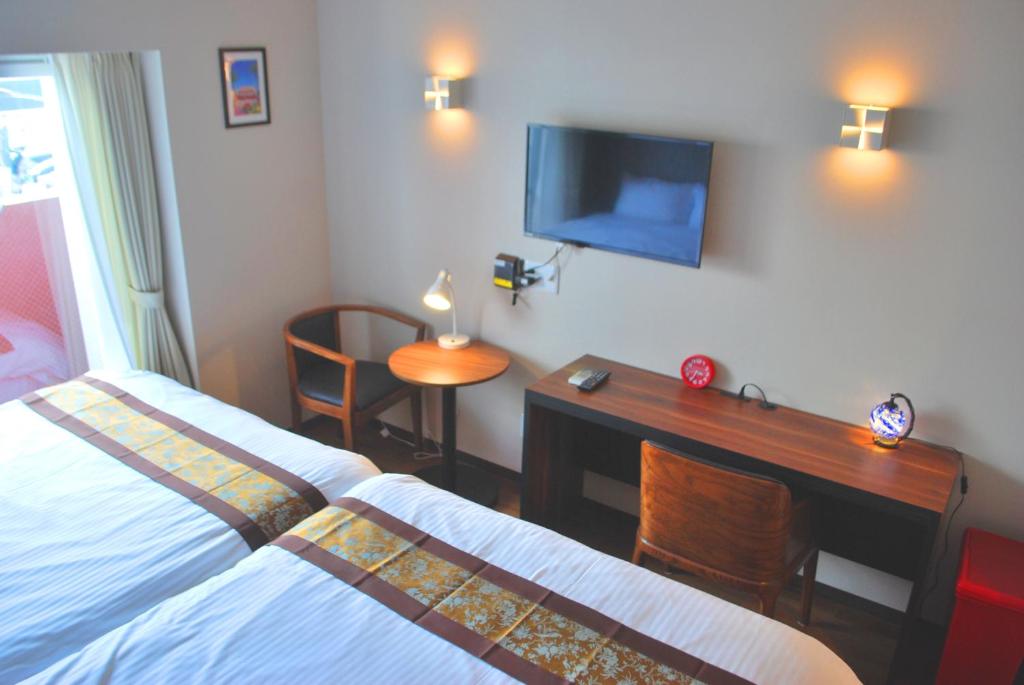 Schlafzimmer mit einem Schreibtisch, einem TV und einem Bett in der Unterkunft Ten Point Hotel Airport in Naha