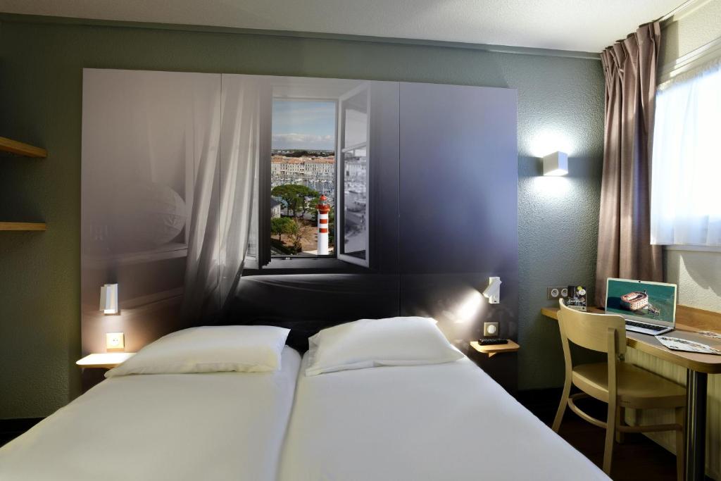 a bedroom with two beds and a desk and a window at B&B HOTEL La Rochelle Angoulins in Angoulins-sur-Mer