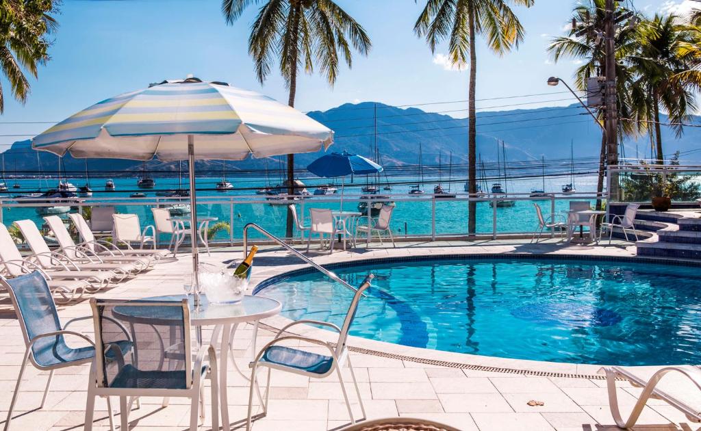 uma piscina com mesas e cadeiras e um guarda-sol em Hotel Ilhabela em Ilhabela