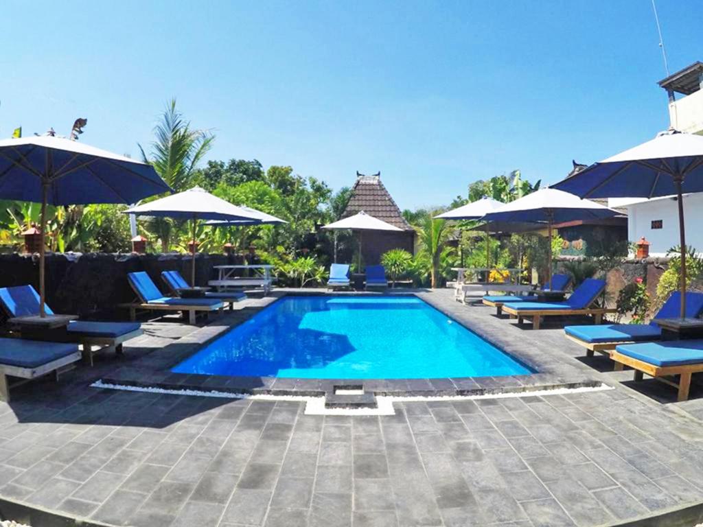a swimming pool with chairs and umbrellas at Colour Cottage in Gili Air