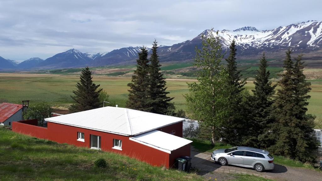 a car parked in front of a red house with mountains at Brúnalaug Guesthouse - Holiday Home in Eyjafjaroarsveit