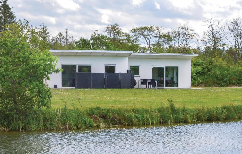 a white house on a lawn next to a body of water at Holiday Home Dyrefolden Ringkøbing Iv in Hee