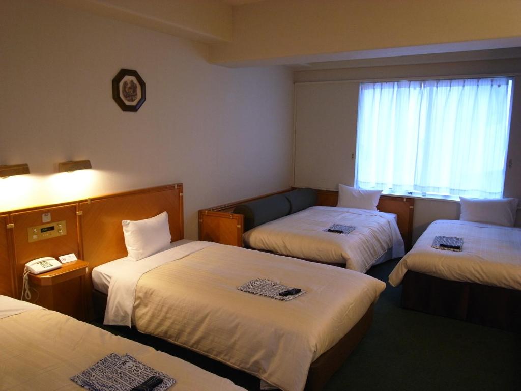 東京にあるホテル機山館のベッド3台と窓が備わるホテルルームです。