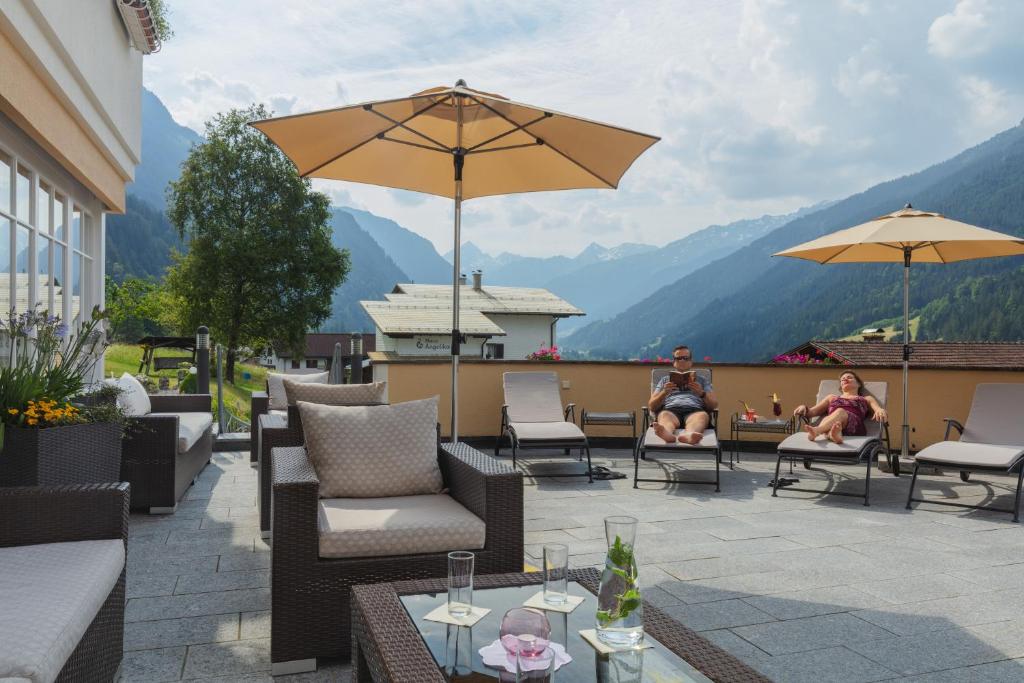 two people sitting on a patio with chairs and umbrellas at Berg-Spa & Hotel Zamangspitze in Sankt Gallenkirch