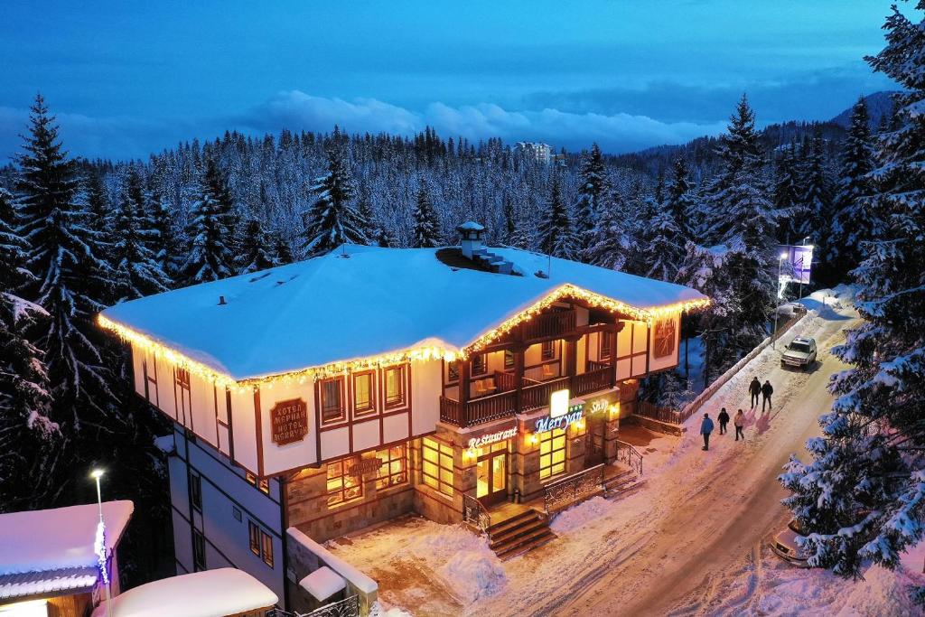 a house in the snow with lights on at MPM Family Hotel Merryan in Pamporovo