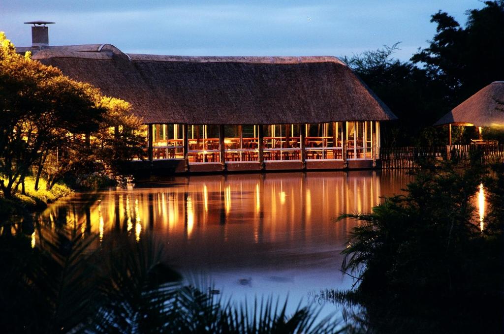 un grand bâtiment avec toit de chaume sur un lac dans l'établissement Premier Resort Mpongo Private Game Reserve, à Macleantown