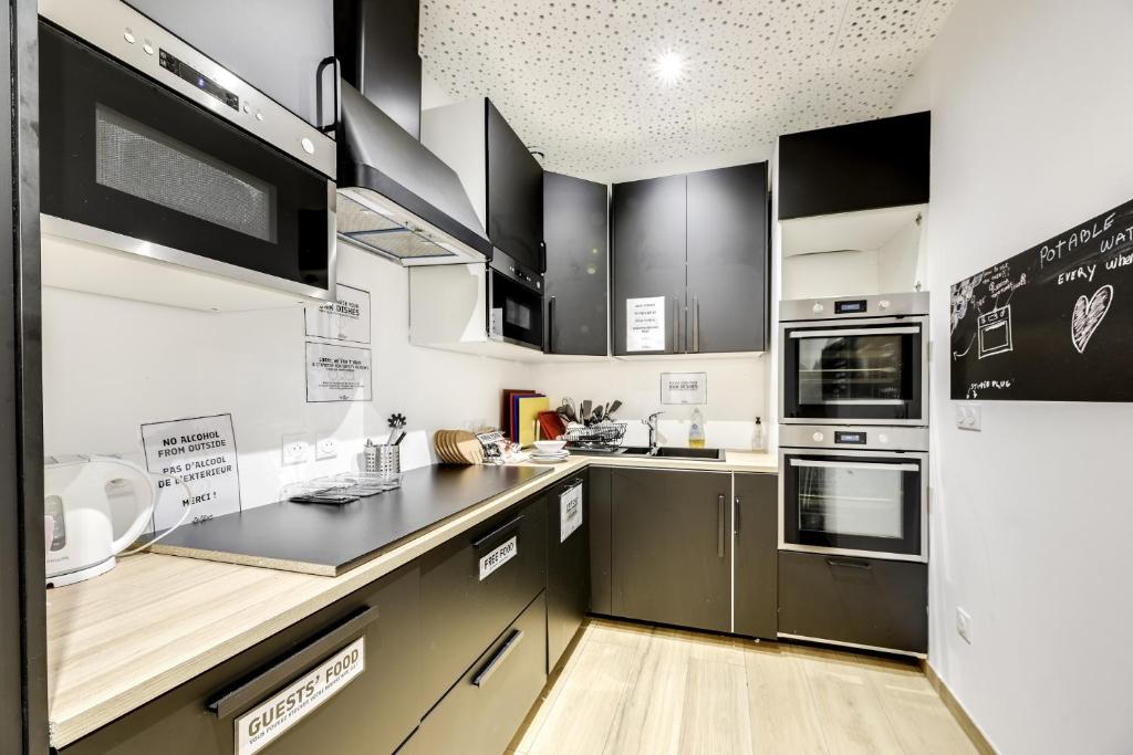 a kitchen with stainless steel appliances and black cabinets at The People - Paris Bercy in Paris