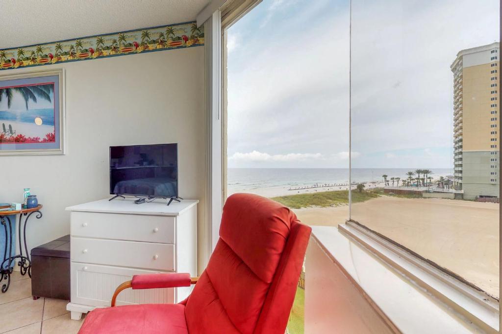 a room with a red chair and a window with a view of the beach at The Top of the Gulf #612 in Panama City Beach