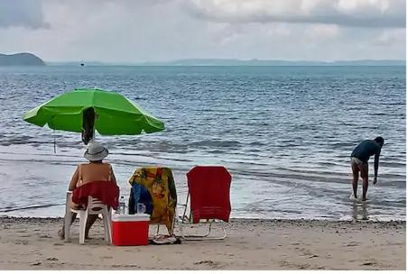 dwoje ludzi siedzących na plaży pod zielonym parasolem w obiekcie Casa Ilha de Itaparica w mieście Itaparica