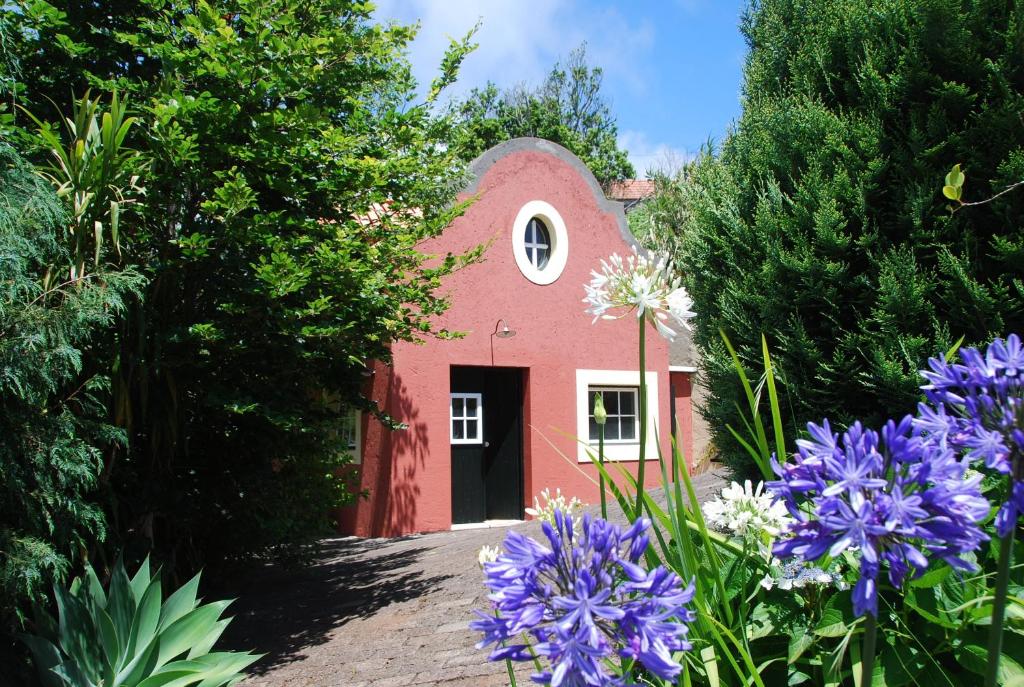 een rood gebouw met een zwarte deur en paarse bloemen bij Casa Da Muda in Ponta do Pargo