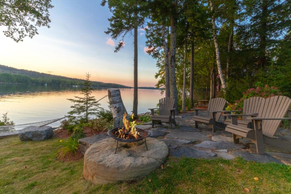 a fire pit with chairs and a table and a lake at Lodge at Moosehead Lake in Greenville Junction