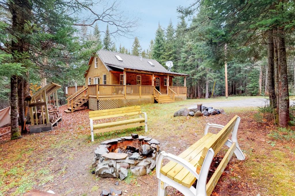 uma cabana de madeira na floresta com bancos e uma lareira em Maine Attraction em Upper Shirley Corner