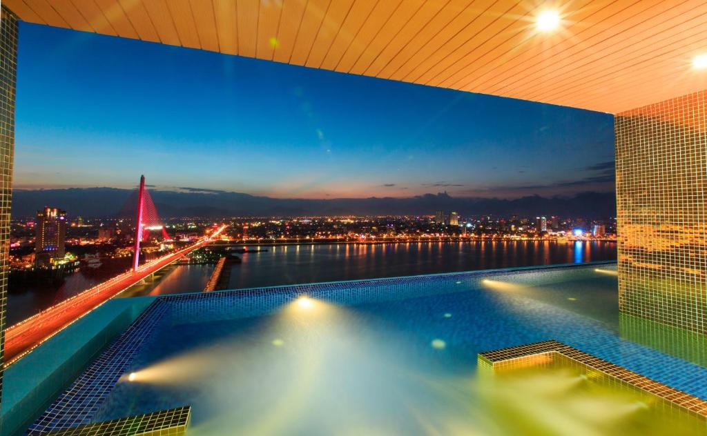 A rooftop pool at dusk overlooking a lit riverfront city and bridge.