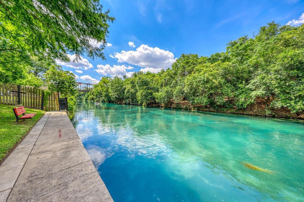 a river with blue water and a bench on a pathway at River Run in New Braunfels