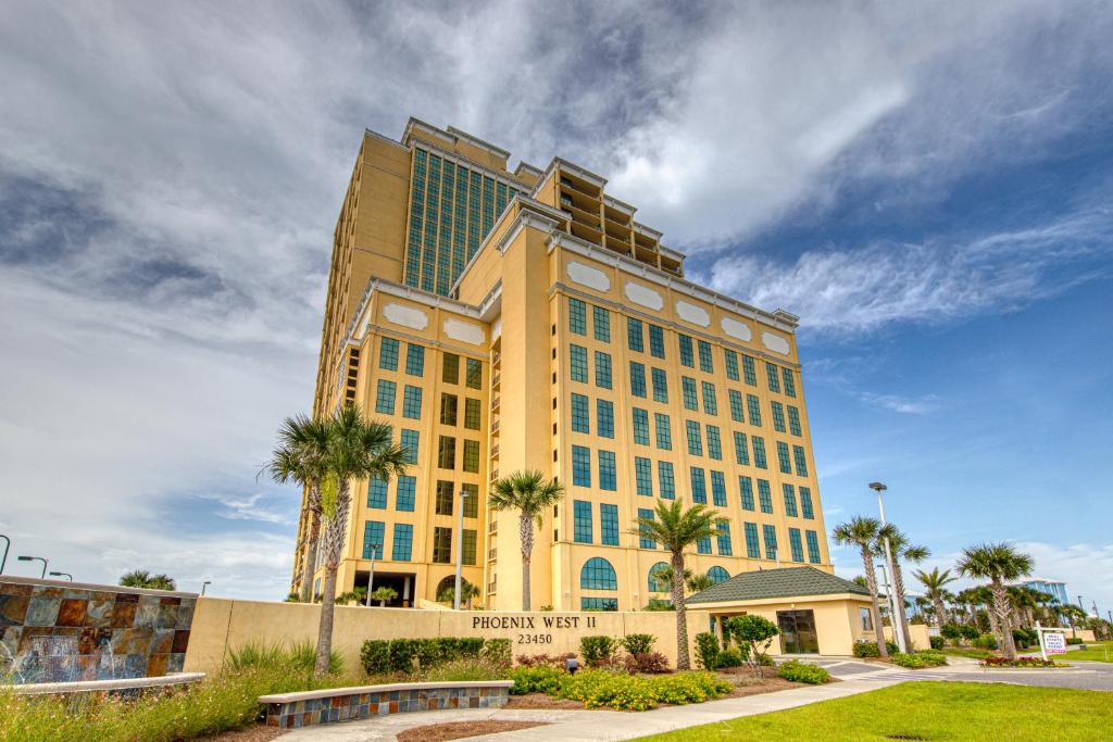 un grand bâtiment jaune avec des palmiers devant lui dans l'établissement Phoenix West II #1916, à Orange Beach