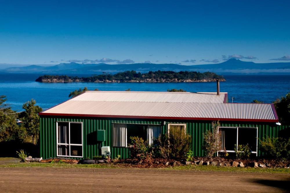 a green building with a red roof next to the water at Discover Bruny Island Holiday Accommodation in Alonnah