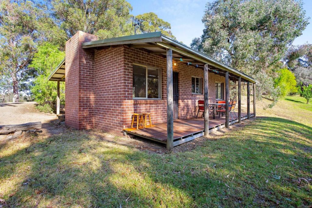 a brick house with a porch and a deck at Braeside Cabin Three Parsonsia in Central Tilba