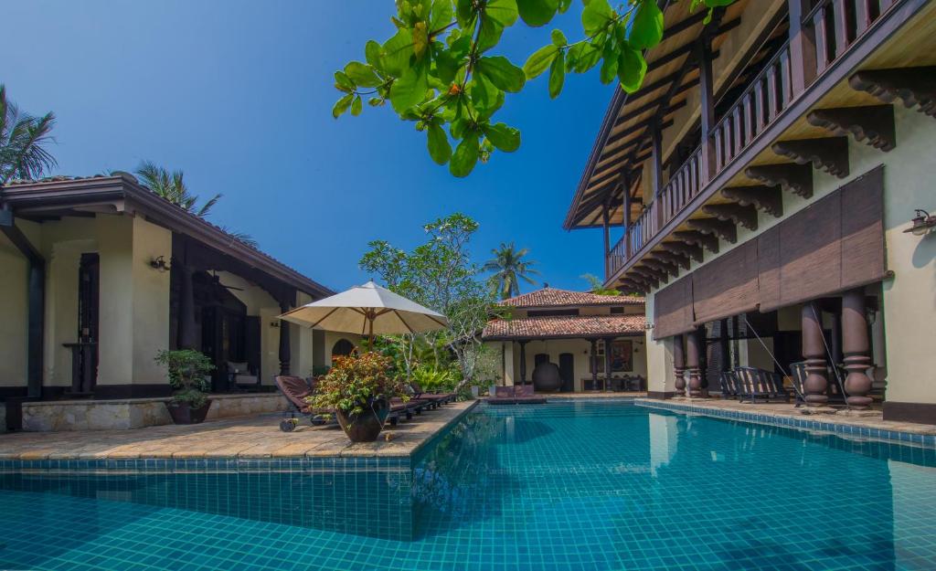 a swimming pool next to a building with an umbrella at Sergeant House Boutique Villa & Private Beach in Unawatuna